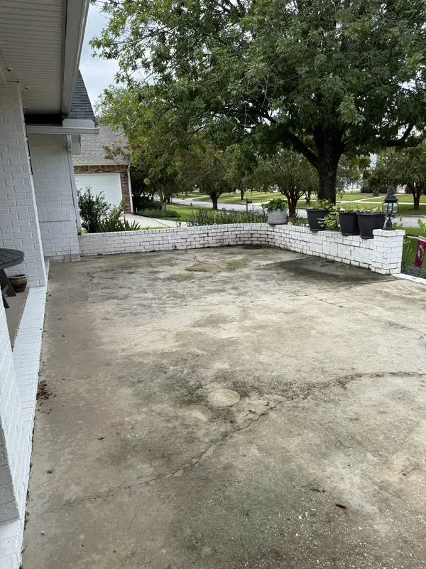 Concrete patio beside a white brick home before pressure washing
