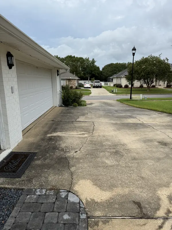 Dark buildup on a concrete driveway beside a white garage before pressure washing